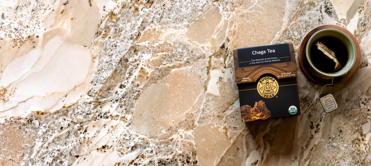 A box of Chaga Tea and a brewed cup of tea sit on a beige and brown marbled stone surface.