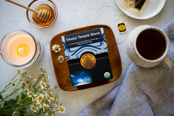 Sleepy Temple Blend on a wooden tray with a lit candle, flowers, and a mug of tea.