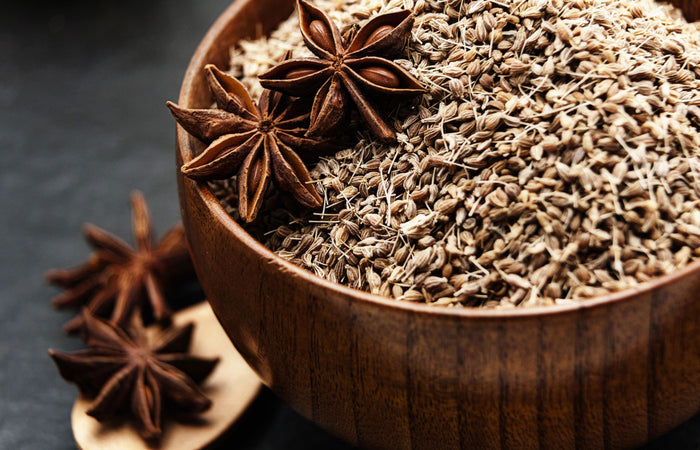 Wooden bowl filled with star anise and anise seeds on a dark background
