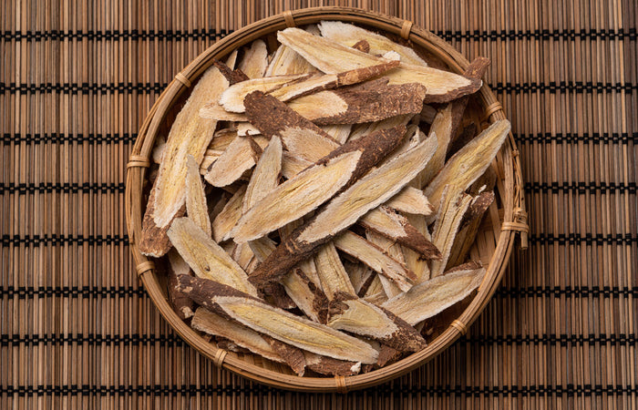 Dried astragalus herbs in a woven basket on a wooden mat
