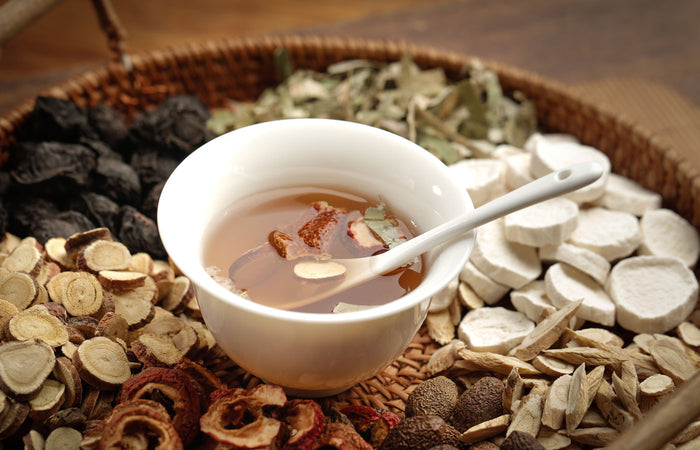 Tea cup with herbs and slices of astragalus root on a woven tray