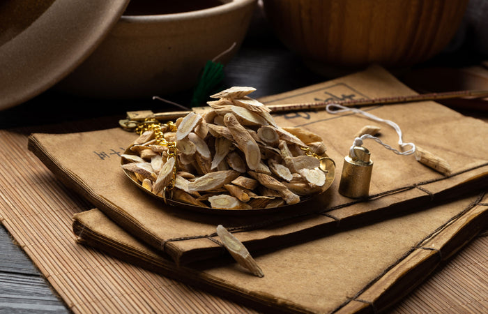 Dried astragalus roots on a wooden surface with a small bottle and bowl in the background.