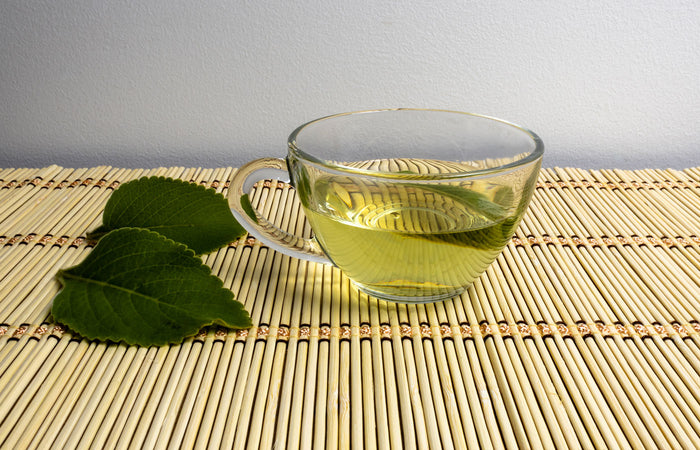Clear glass cup of bilberry tea with bilberry leaves on a bamboo mat