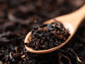 Wooden spoon filled with black tea leaves on a dark background
