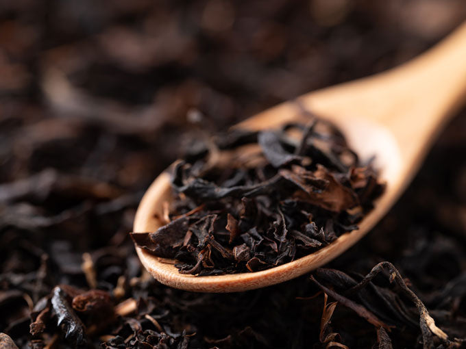 Wooden spoon filled with black tea leaves on a dark background
