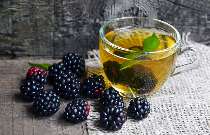 Glass mug of blackberry iced tea with fresh blackberries on a wooden surface