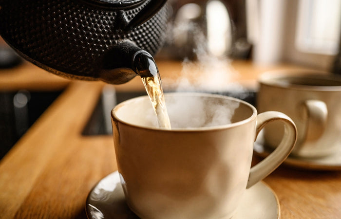 Tea being poured from a teapot into a white mug on a wooden table.