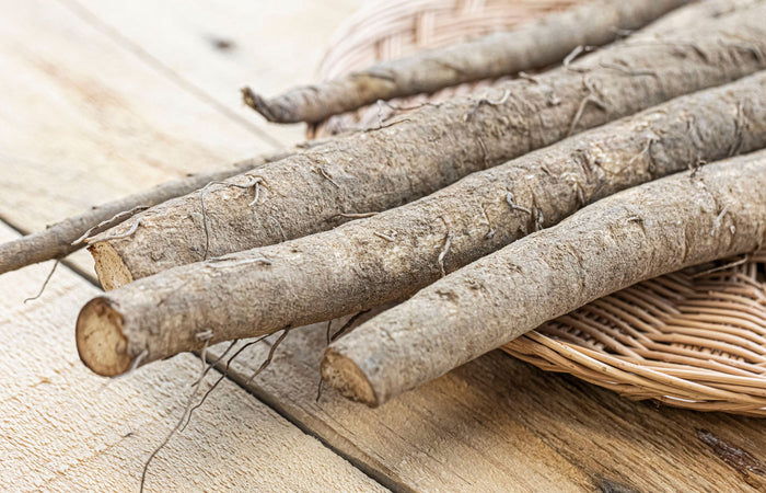 Close-up of burdock root on a wooden surface with a woven basket in the background.