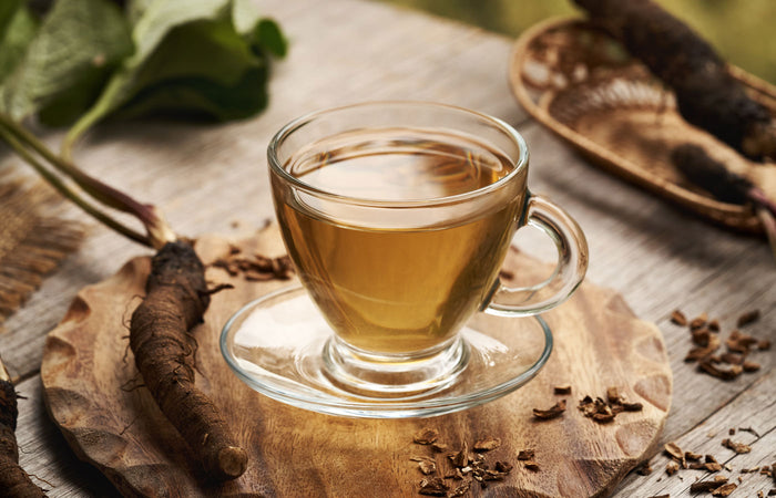 Glass cup of burdock root tea on a wooden surface with tea leaves and a spoon.