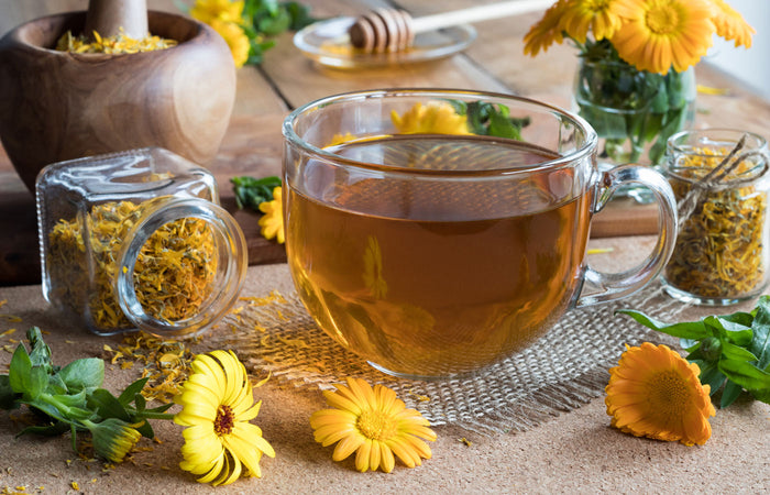 Glass mug of tea with dried herbs and calendula flowers on a wooden surface