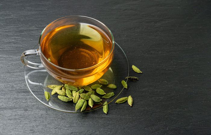 Clear glass cup of tea with green cardamom pods on a dark slate surface