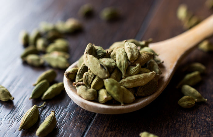 Cardamom pods on a wooden spoon and scattered on a dark wooden surface