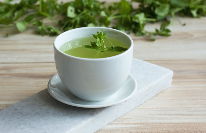 White cup of chickweed  tea on a wooden surface with leaves in the background