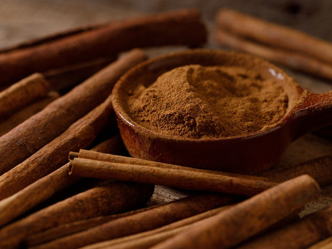 Wooden spoon filled with cinnamon powder surrounded by cinnamon sticks on a wooden surface