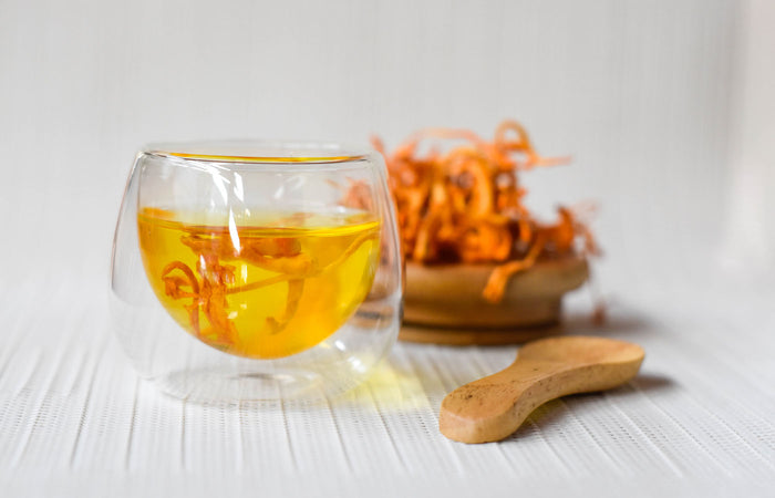 Glass cup with cordyceps tea and a wooden spoon on a light surface