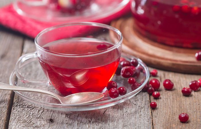 Clear glass cup filled with red cranberry tea on a wooden surface with scattered cranberries.