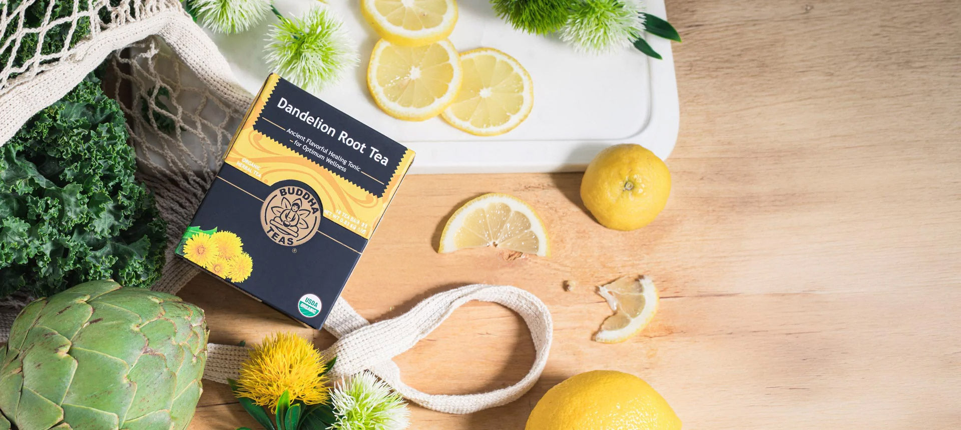 Dandelion root tea package with lemons, kale, artichokes, and a knife on a wooden surface.