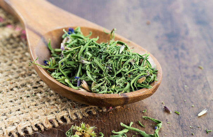Wooden spoon filled with green dried hyssop on a wooden surface