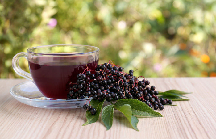 Clear glass cup of tea with elderberries and leaves on a wooden surface