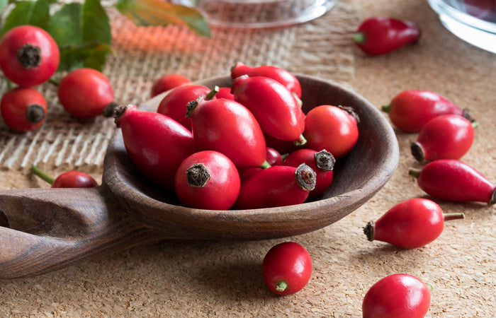 Red rose hips in a wooden spoon on a textured surface