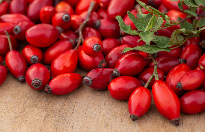 Close-up of red rose hips with green leaves on a wooden surface