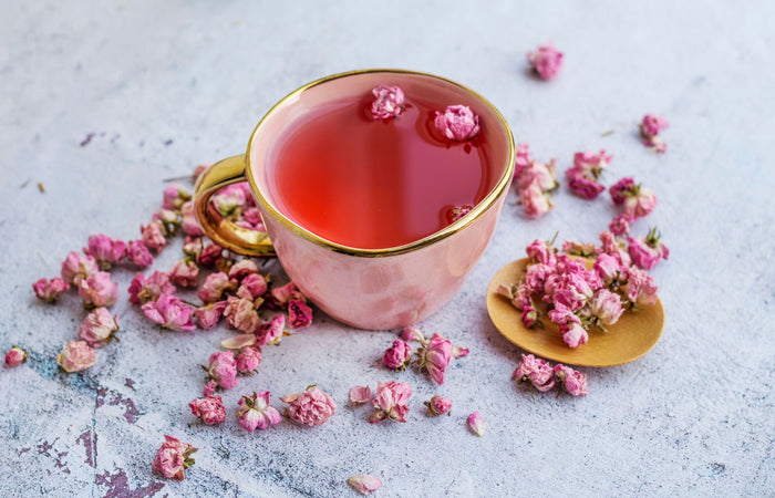 Pink floral tea in a gold-rimmed cup with scattered flowers on a light surface