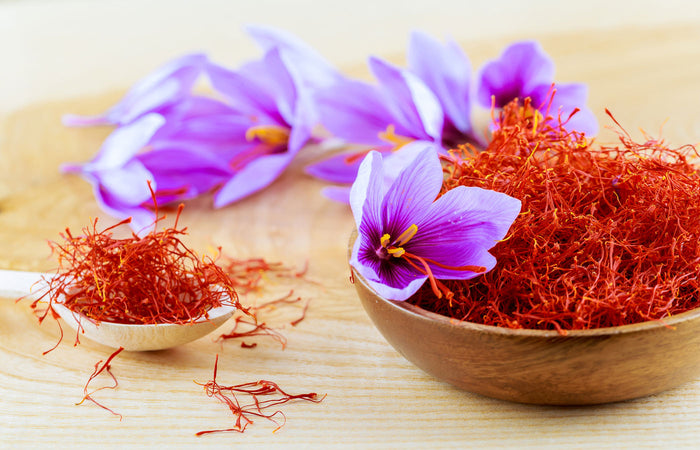 Saffron threads and flowers in wooden bowls on a wooden surface