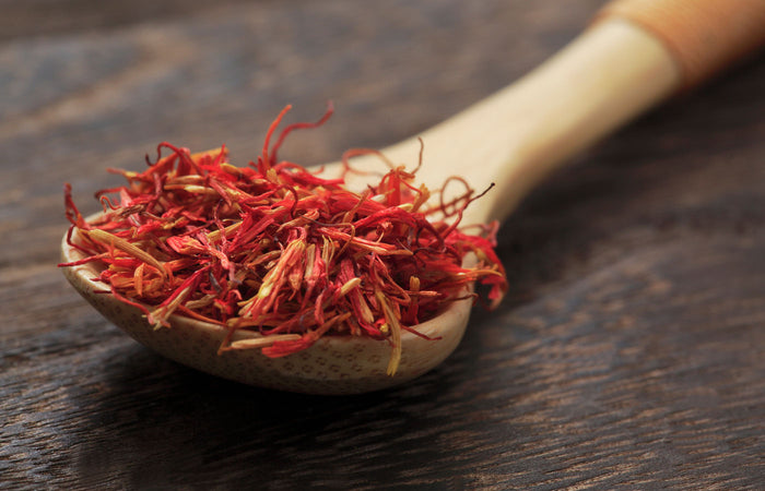 Dried saffron on a wooden spoon against a dark wooden background
