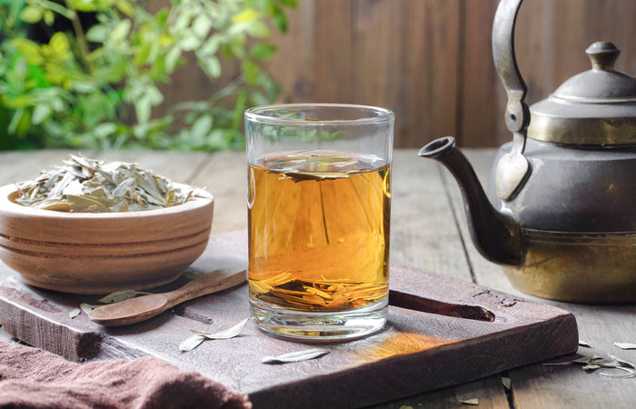 Glass of tea with a teapot and bowl of Senna  leaves on a wooden surface