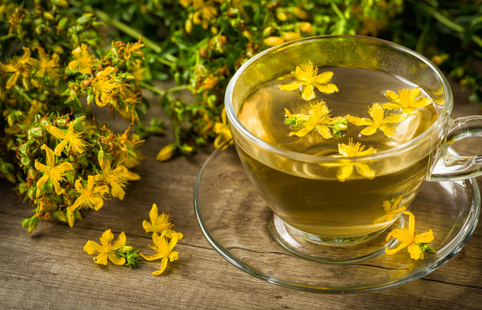 Glass cup of St John's Wort  tea on a wooden surface with fresh flowers.