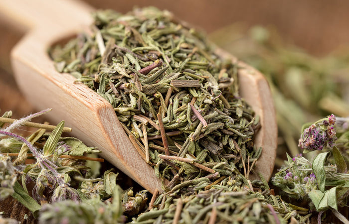 Wooden scoop filled with dried green thyme herbs.