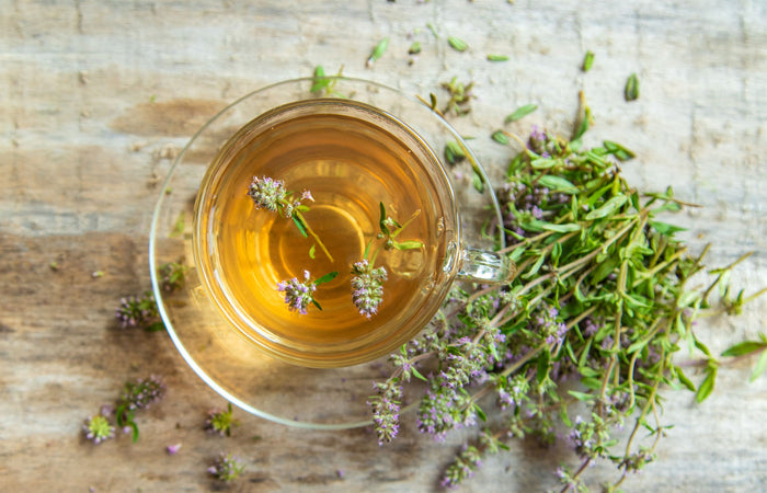 Clear glass mug filled with Thyme leaf tea on a wooden surface with fresh herbs.