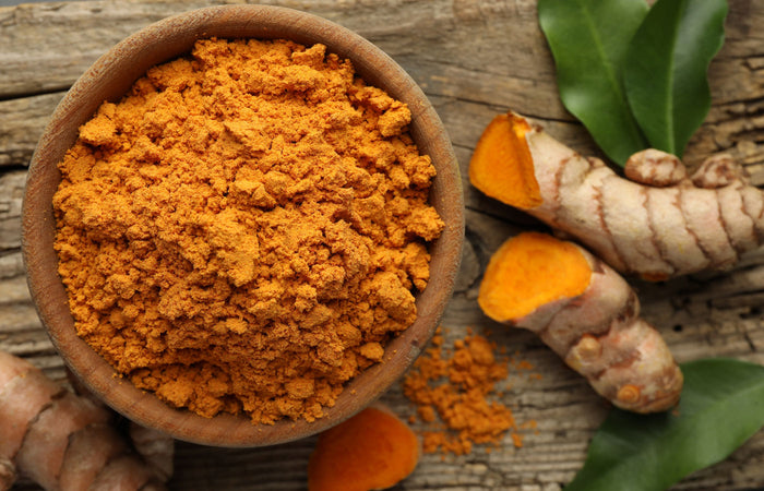 Turmeric powder in a bowl with turmeric roots and leaves on a wooden surface