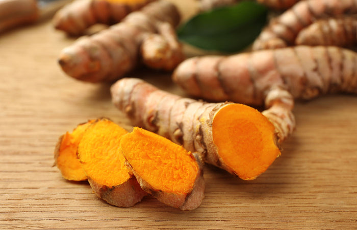 Turmeric roots with a few sliced pieces on a wooden surface