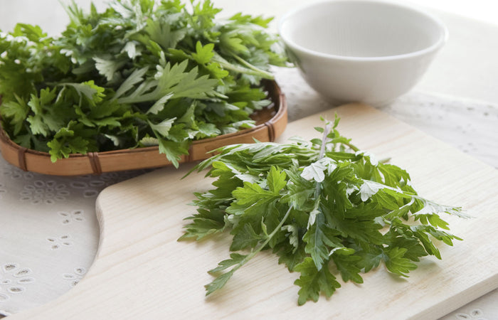 Fresh green wormwood on a wooden cutting board with a white bowl in the background.