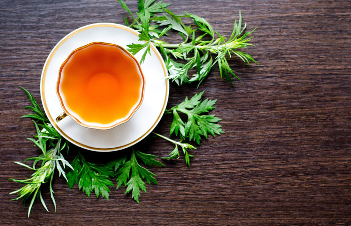 Tea cup with green wormwood leaves on a wooden surface