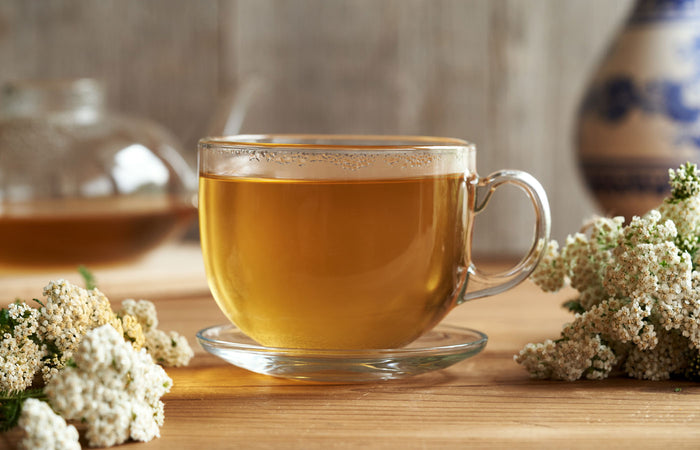 Clear glass mug filled with yarrow tea  on a wooden surface with yarrow flowers.