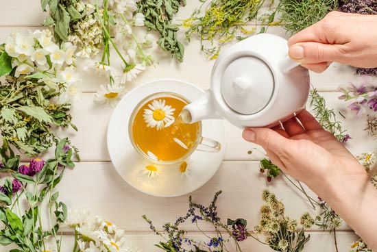 Woman pouring chamomile herbal tea on white wooden background.